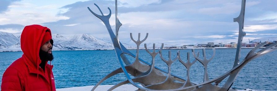 In a red jacket beside the Sun Voyager sculpture in Reykjavík, Iceland